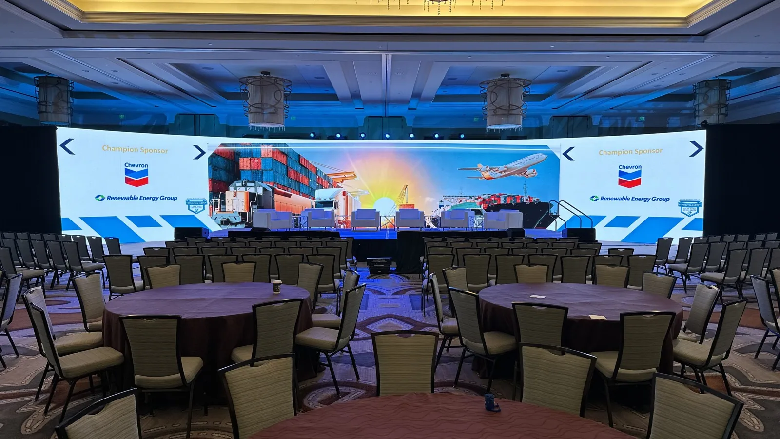 Wide hotel ballroom with a large sponsor LED wall, full staging, and rounds set for a produced corporate show
