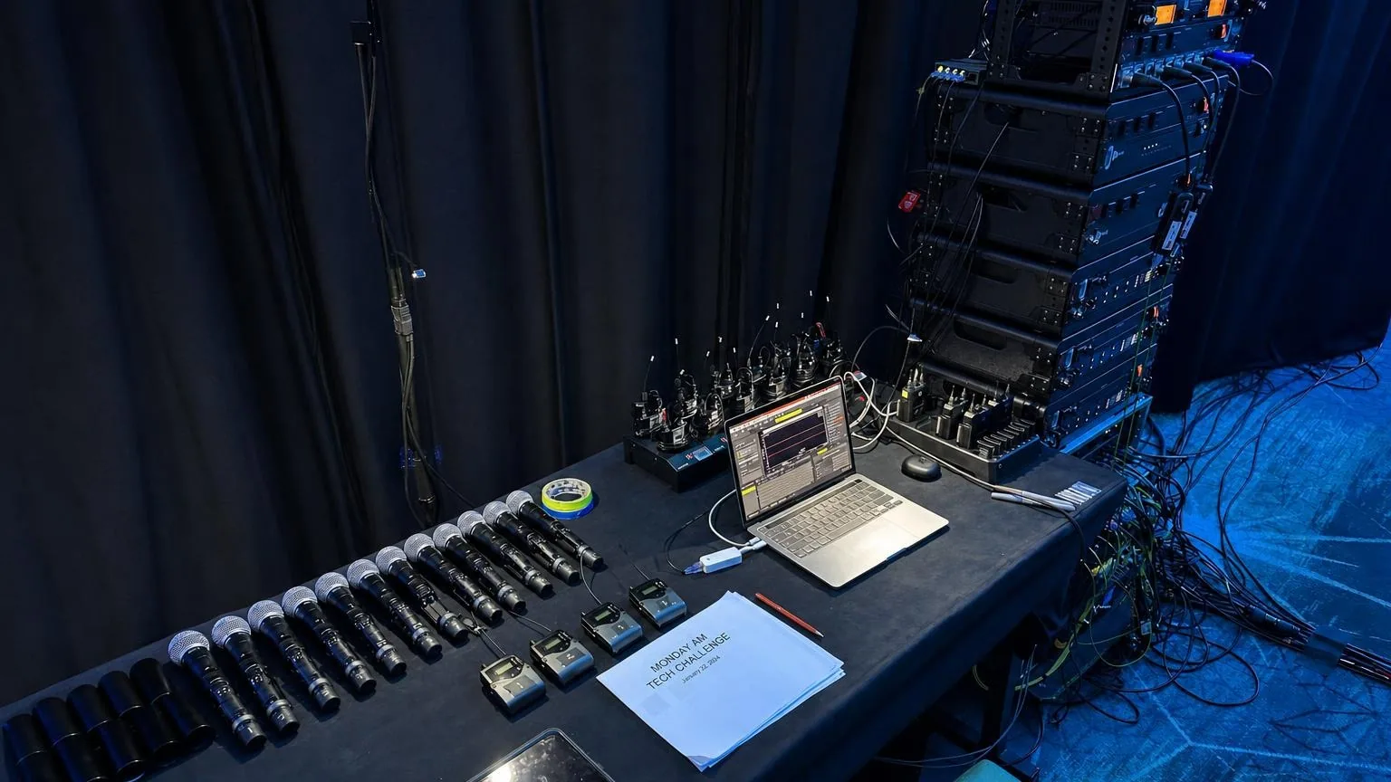 Wireless microphone receivers, belt packs, and RF coordination laptop at a corporate event tech table